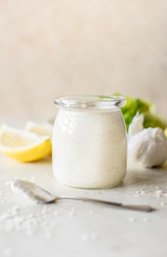 a glass jar filled with white liquid next to sliced lemons and broccoli