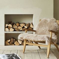 a chair sitting in front of a fire place filled with logs and a book on the floor