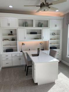 a white desk with two chairs and a ceiling fan in a room that has built - in bookcases