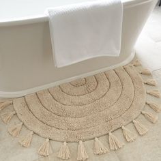 a white bath tub sitting next to a rug with tassels on the floor