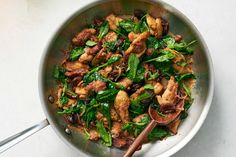 a pan filled with chicken and spinach on top of a white countertop next to a wooden spoon