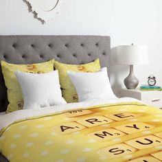 a bed covered in yellow and white sheets with scrabble letters on it, next to a clock