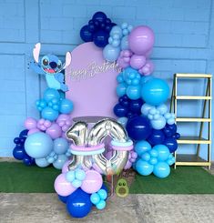 balloon decorations and balloons are arranged on the ground in front of a blue brick wall