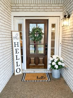 a welcome mat on the front door of a house with white flowers and a wreath