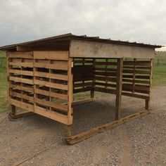 a wooden shelter sitting on top of a dirt road next to a green grass covered field