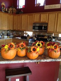 four pumpkins decorated with flowers sit on a kitchen counter