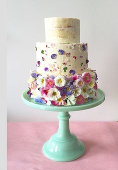 a three tiered cake with white frosting and multi colored flowers on a green plate