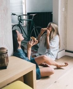 two women sitting on the floor eating pizza