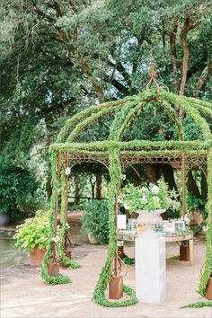 a gazebo covered in greenery and potted plants for an outdoor wedding ceremony