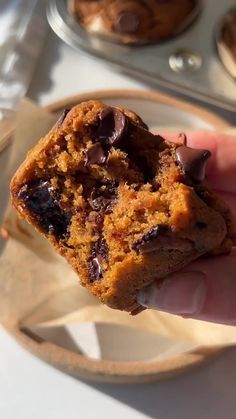 a hand holding a chocolate chip cookie in front of muffins