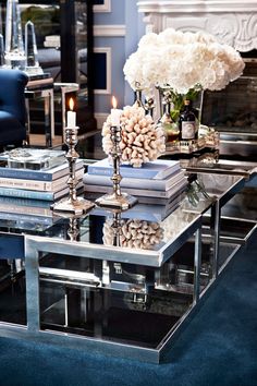 a glass table topped with lots of books next to a blue chair and fire place