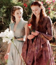 two young women dressed in medieval clothing standing next to each other, one holding a flower