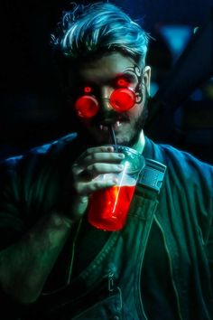 a man with red eye glasses drinking from a drink in front of his face and holding a straw