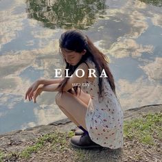 a woman sitting on the ground next to a body of water with her legs crossed