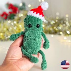 a hand holding a green stuffed animal with a santa hat on it's head