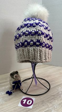 One-of-a-kind, ready-to-ship, handmade winter hat/beanie.  Bursting with color, this white, and purple beanie features a 5" white, faux fur, removable PomPom.  Made of fine Malabrigo Rasta wool yarn, this beanie must be hand washed and dried flat to preserve its softness and durability.  The hat measures 8" across and 8" tall allowing the wearer to pull it down over the ears or roll it up depending on the required warmth.  Knit from my own original design, The Poppy Hat pattern is available on Ravelry for the adventurous beginning knitter.  As with any handmade item, minor flaws and imperfections are inherent to its construction and adds a unique charm to the finished project. Knitted Chunky Hat Free Pattern, White Adjustable Beanie For Cold Weather, Adjustable Purple Beanie For Winter, White One-size Bonnet For Cold Weather, One Size White Bonnet For Cold Weather, White One Size Bonnet For Cold Weather, White Yarn Bonnet For Winter, Winter White Yarn Bonnet, White Crochet Beanie Hat As Gift