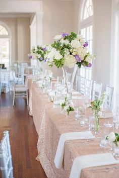 a long table is set up with white and purple flowers in vases on it