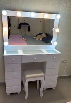 a white vanity with lights on it and a stool in front of the mirror that is lit up