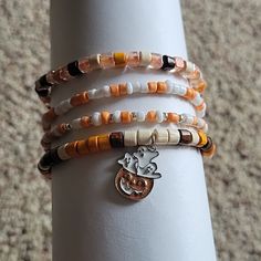 Handmade Halloween Stretch Bracelets. Four Bracelets Total. Colors Are White, Cream, Brown, Orange And Silver With A Pumpkin And Ghost Charm. Halloween Inspired Bracelets, Halloween Stretch Bracelets, Beaded Bracelets Fall, Heishi Bracelet Ideas Fall, Autumn Bracelet Ideas, Fall Beaded Jewelry, Fall Beaded Bracelets, Fall Bracelet Ideas, Halloween Bracelet Ideas