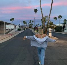 a woman is walking down the street with her arms outstretched in front of palm trees