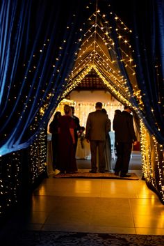 people are walking down the aisle covered in lights and blue drapes at night