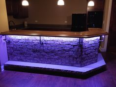 a bar made out of bricks with lights on the top and purple lighting around it