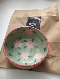 a pink and green bowl sitting on top of a table next to a brown paper bag