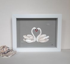 two white swans in a shadow box with a heart on the front and one behind it