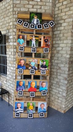 a tall wooden shelf with pictures on it in front of a brick wall and window