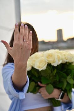 a woman with her hand up to the camera holding flowers in front of her face