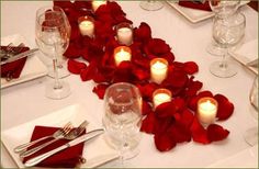 the table is set with red rose petals and candles in the shape of a heart