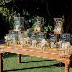 a wooden table topped with lots of vases filled with white flowers and greenery