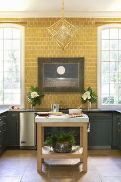 a kitchen with yellow brick walls and green cabinets, an island in front of the sink