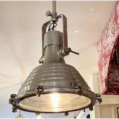 an industrial light hanging from the ceiling in a room with white walls and red drapes