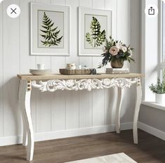 a white table with two pictures on the wall behind it and a vase filled with flowers