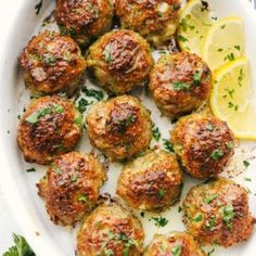 a white plate topped with meatballs and lemon wedges