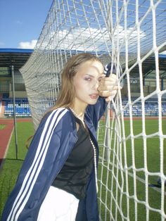 a woman standing next to a soccer goal holding her hand on the side of the net