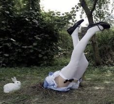 a woman laying on the ground with her legs up next to a white rabbit in a field