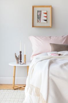 a white bed with pink sheets and two candles on the end table next to it