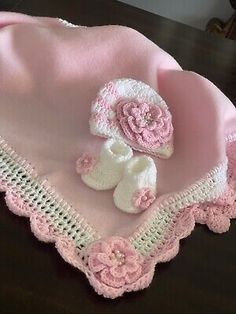 a crocheted hat and booties are sitting on a table with a pink blanket