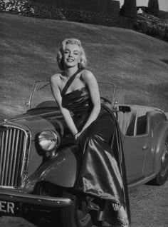 a woman in a dress sitting on the hood of a car