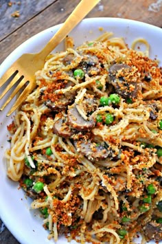 a white plate topped with pasta covered in mushrooms and peas next to a gold fork