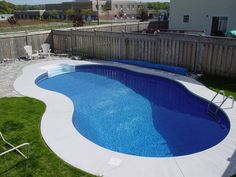 an above ground swimming pool surrounded by lawn chairs and grass in a backyard with a wooden fence