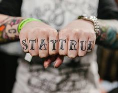 a person with tattoos on their hands holding the word stay true