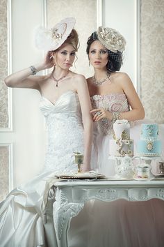 two women in dresses and hats standing next to each other near a table with cake on it