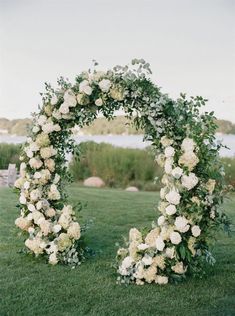 an outdoor wedding ceremony setup with white flowers and greenery on the grass near water