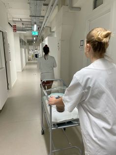 two women in white coats walking down a hospital hallway with a bed on the floor