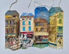 two tags with watercolor paintings of buildings and boats on the river in front of them