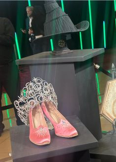 a display case with pink shoes and a hat on it's head, in front of green lights