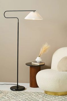 a floor lamp next to a white chair and table with a book on it in a living room